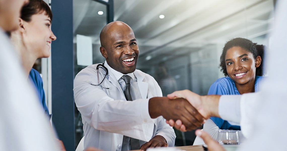 Doctor shaking hands with another doctor amongst other doctors and nurses